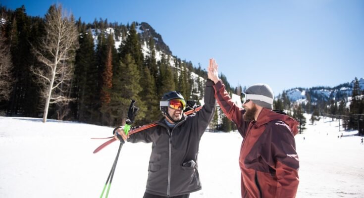 Two friends high-fiving while skiing.