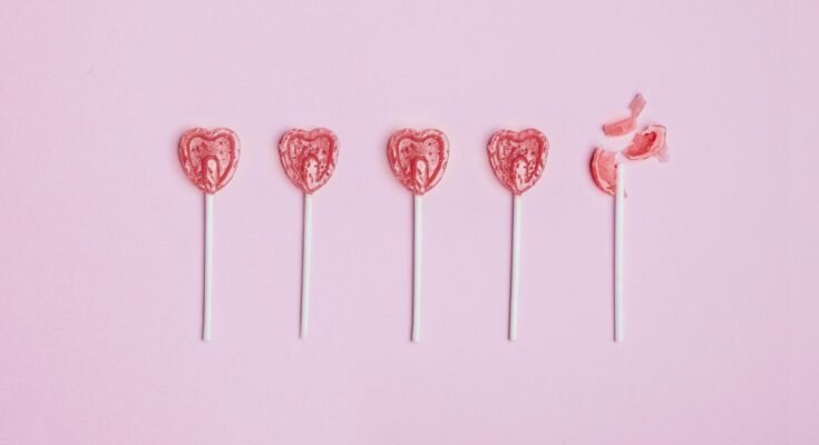 Five lollipop hearts on a pink floor, but the last one is smashed to pieces.