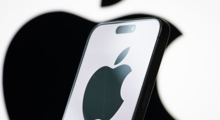 In this photo illustration, the logo of Apple Inc. is displayed on a smartphone screen, with the company's iconic black apple symbol visible in the background.