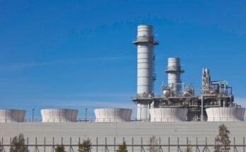 Smoke stacks from a natural gas power plant stand against a blue sky.