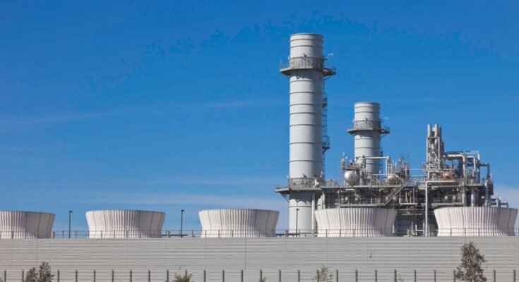 Smoke stacks from a natural gas power plant stand against a blue sky.