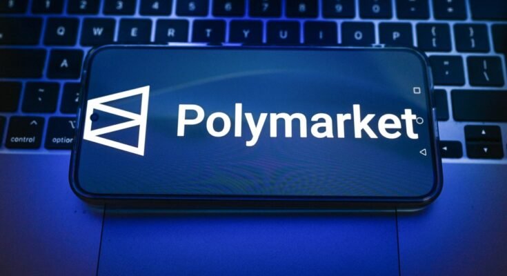 In this photo illustration, a Polymarket logo is displayed on a smartphone on top of a laptop.