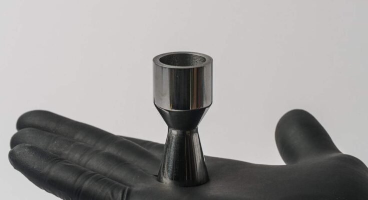 A gloved hand holds a metal part shaped like a rocket nozzle.